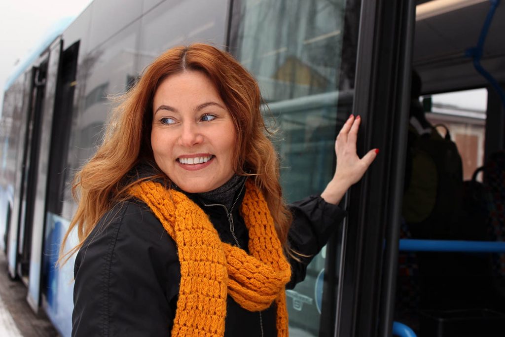 Hymyilevä nainen nousemassa bussiin.